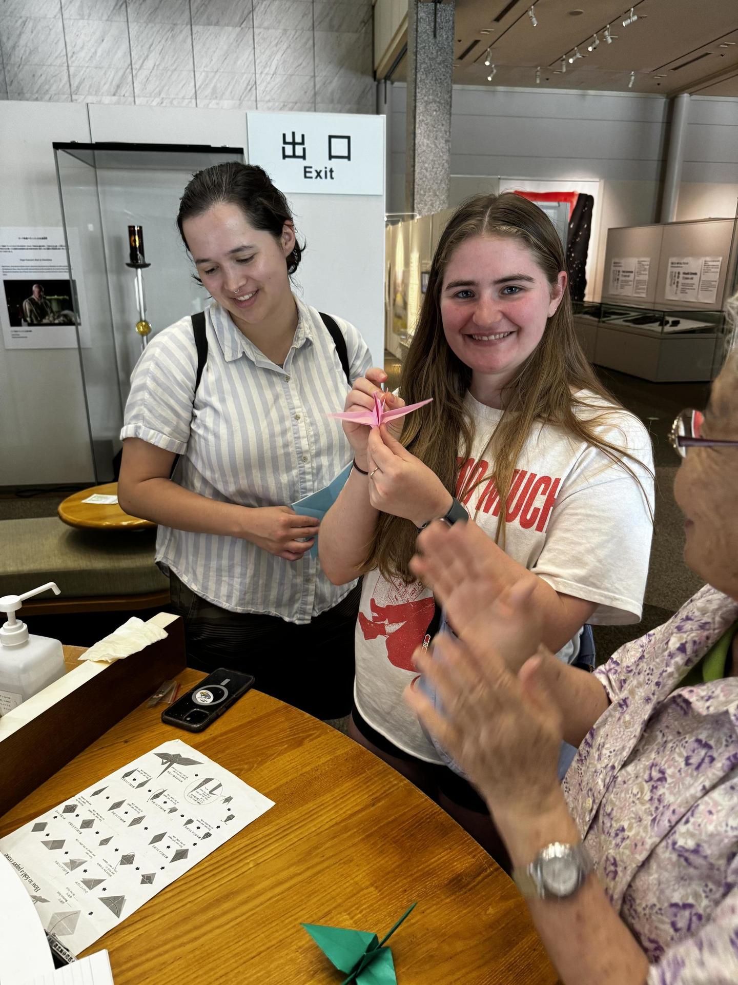 Jessica folding a crane with the help  of an elderly volunteer.
